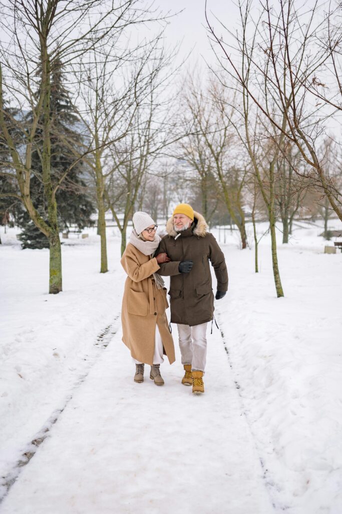 Senior couple in warm clothing walking together on a snowy path in a tranquil park setting.
