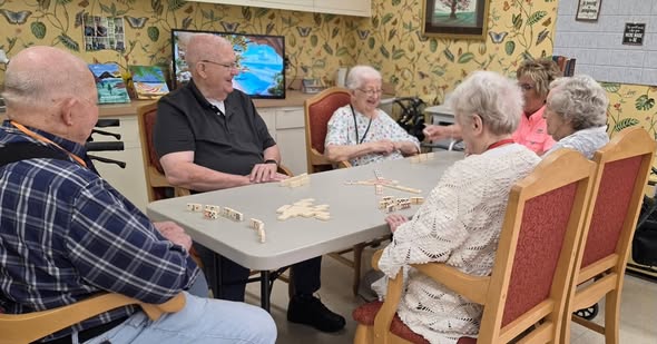 701465340_18010270481885350_6007815475040908744_n Six elderly people are sitting around a table playing dominoes at Wesley Manor, enjoying conversation in a cozy, brightly decorated room. For more about life here, check out the Wesley Manor senior living FAQs.