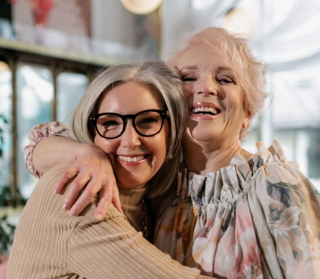 Two senior women hugging joyfully indoors, showcasing friendship and happiness.